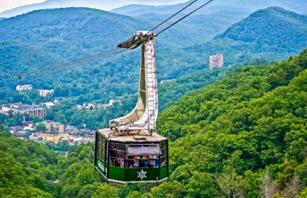A sweeping view from a cable car reveals lush green mountains, the town below, and hints at nearby hiking trails. The scene embodies the natural beauty just beyond the main strip and alludes to the Smoky Mountain National Park's outdoor adventures.