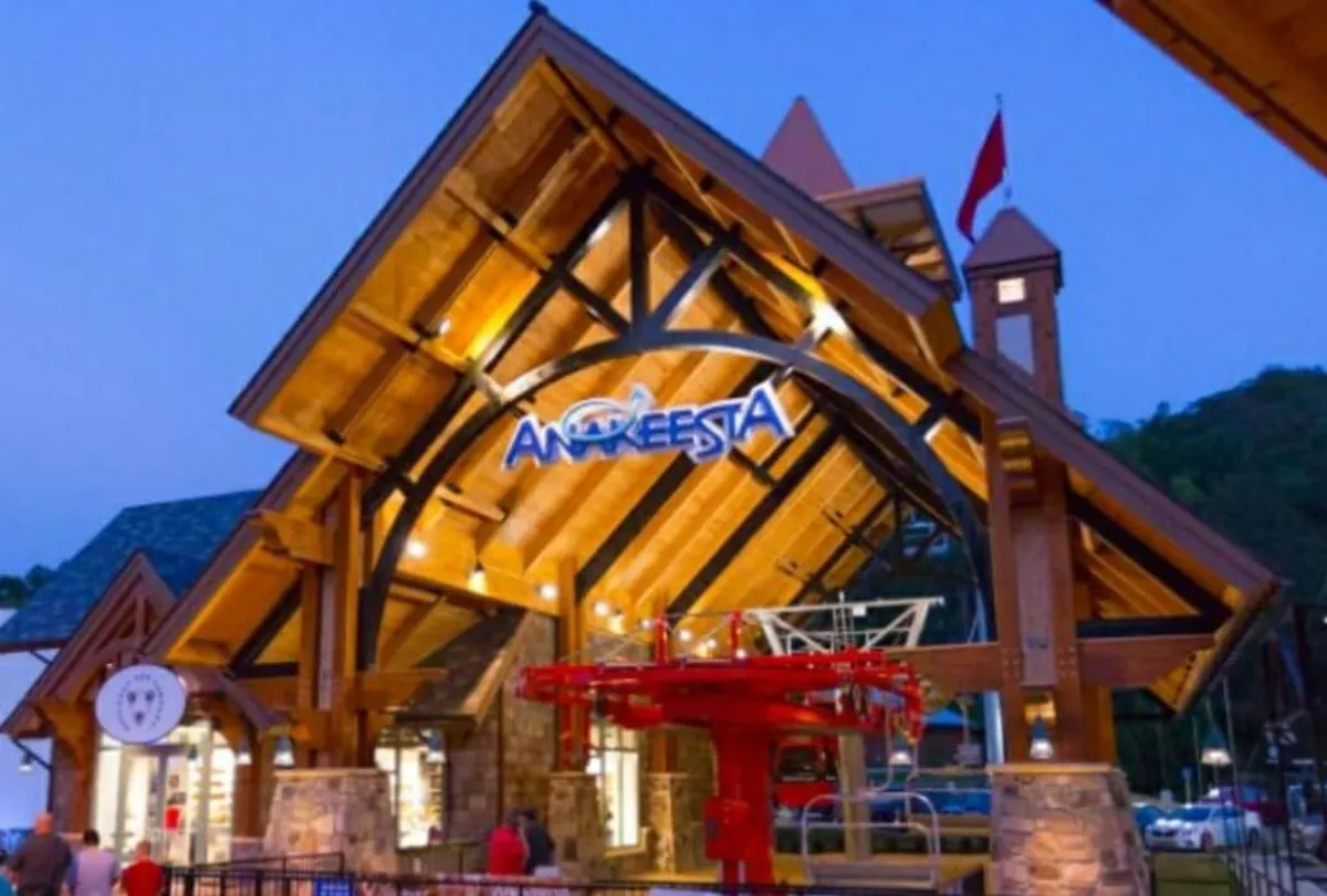 The grand wooden entrance to Anakeesta, with an illuminated sign and a red ski lift visible, welcomes visitors. The atmosphere is festive and bustling, hinting at a variety of attractions, sunset views, and special nighttime events at this popular entertainment hub.