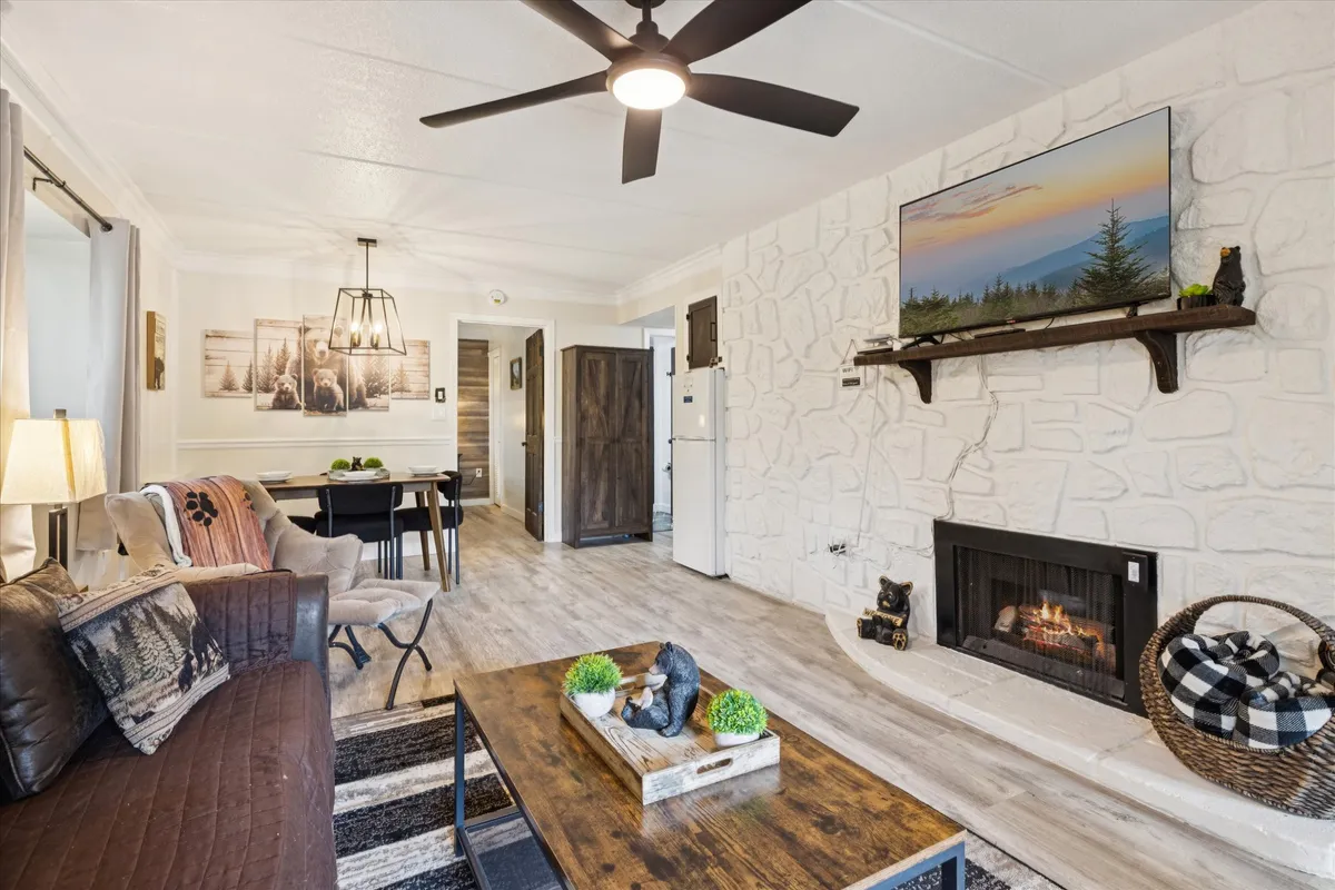 A cozy living room with a stone fireplace, large flat-screen TV, wooden coffee table, and a brown leather couch. The space is warm and inviting, designed for group gatherings and pre-evening drinks before heading out on the town.