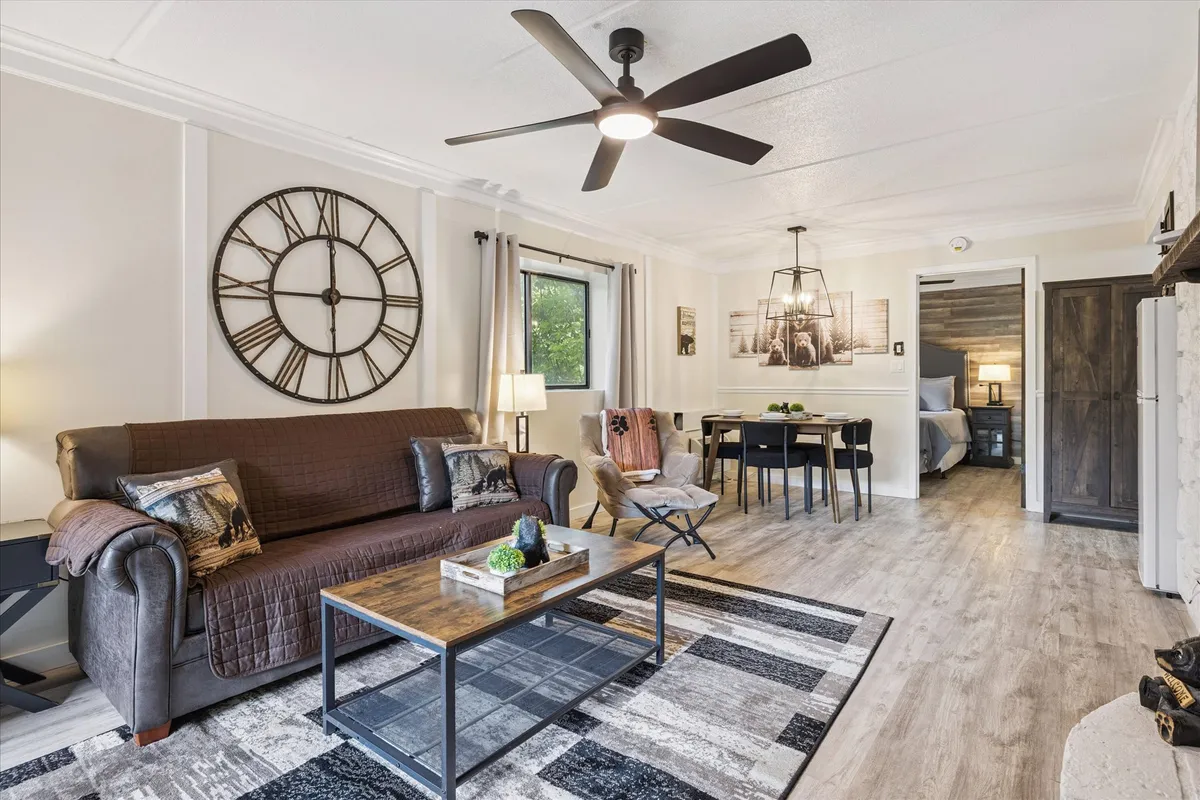 A comfortable and inviting area showing a plush sofa, a stylish coffee table, a prominently displayed large wall clock, and a dining area with a modern pendant light. The space feels cohesive and is ideal for relaxing, sharing meals, or entertaining.