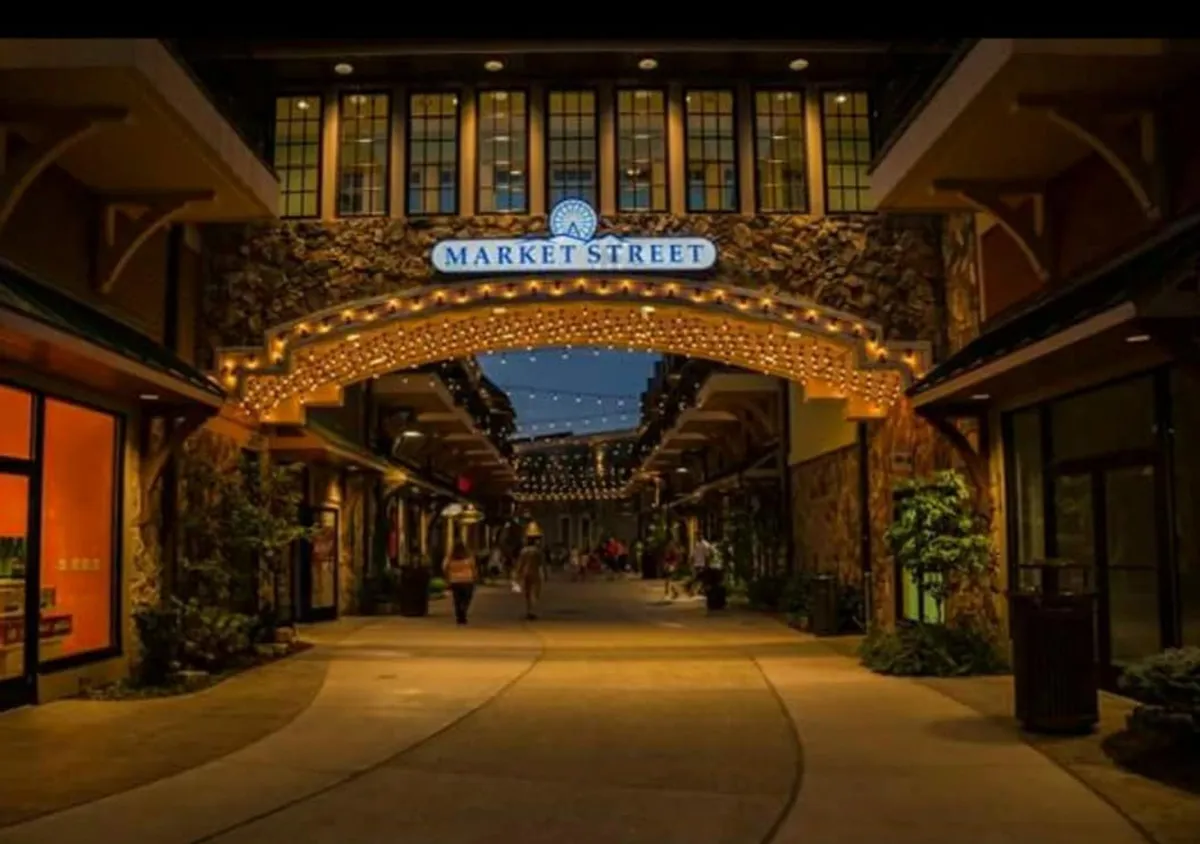 A charming streetscape featuring an arched sign reading 'MARKET STREET,' strung with warm, festive lights overhead. Storefronts glow with inviting lighting, creating a magical ambiance ideal for evening strolls. The cobblestone path and bustling yet cozy atmosphere evoke a sense of romance and discovery.