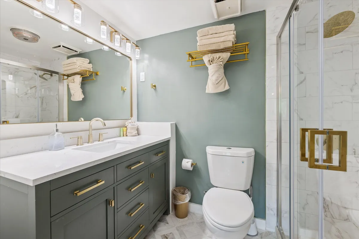 A modern bathroom with a double vanity topped by a marble countertop, accented with gold fixtures and neatly arranged towels. The design is bright, clean, and spa-like, offering a sense of sophistication and relaxation.